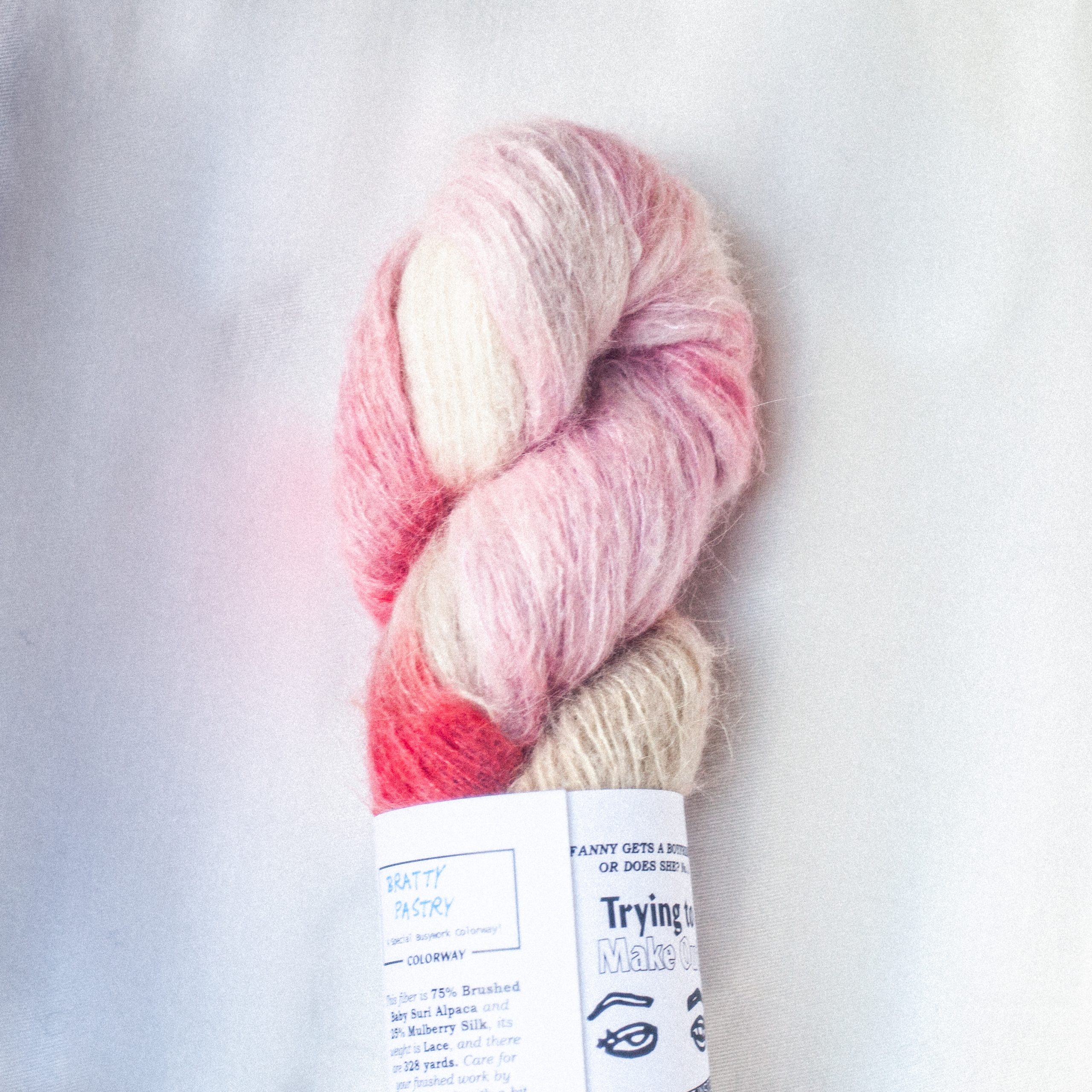 A fluffy suri alpaca skein with daubs of red-orange, cool pink, royal blue, and sea green on a background of cream and taupe hand dyed yarn