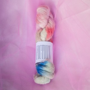 A fluffy suri alpaca skein with daubs of red-orange, cool pink, royal blue, and sea green on a background of cream and taupe hand dyed yarn